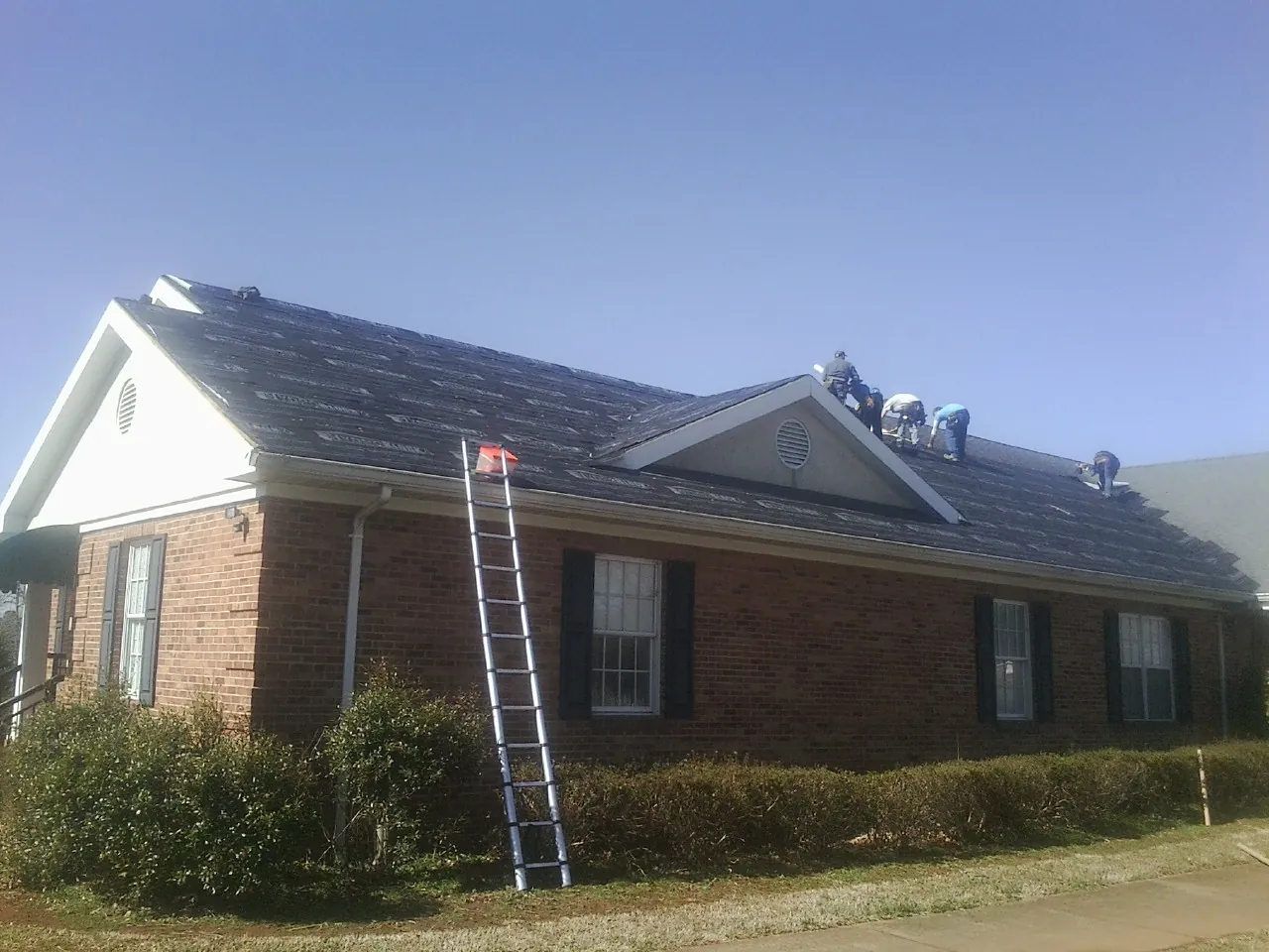 Crew tearing shingles off a brick ranch roof with a ladder set — Metal Roof Repair work by our crew in Exmore