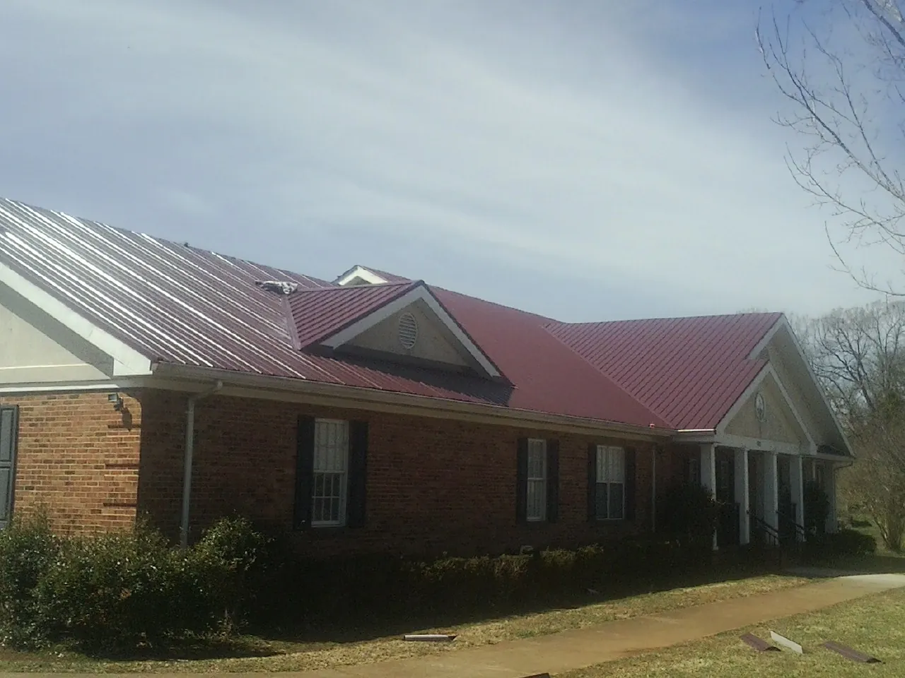 Red metal roof with gabled entries on a long brick building, from a Hail Damage Roof Repair job in Exmore
