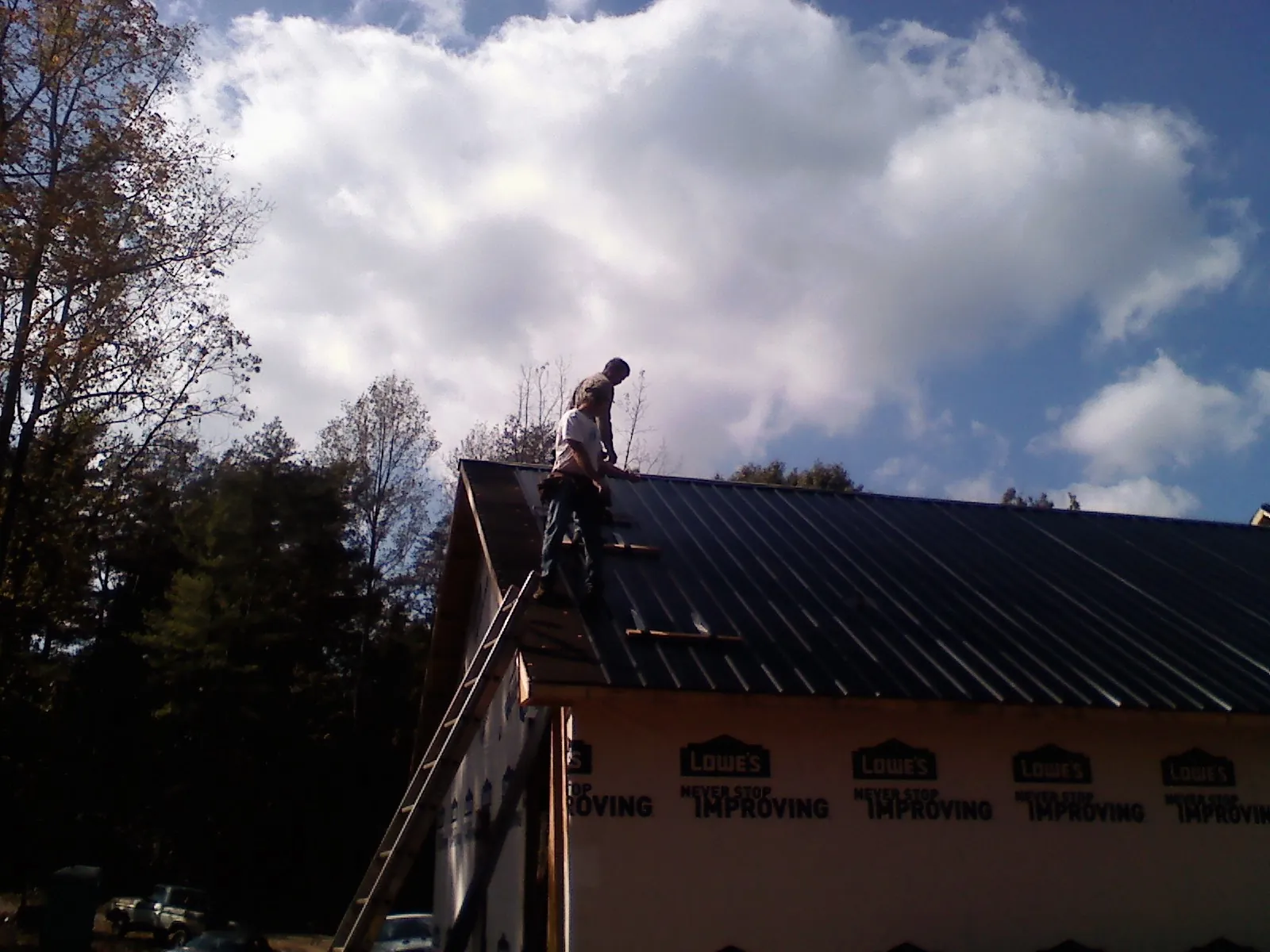Roofer fastening dark metal panels high against a cloudy sky, from a Roof Inspection job in Exmore